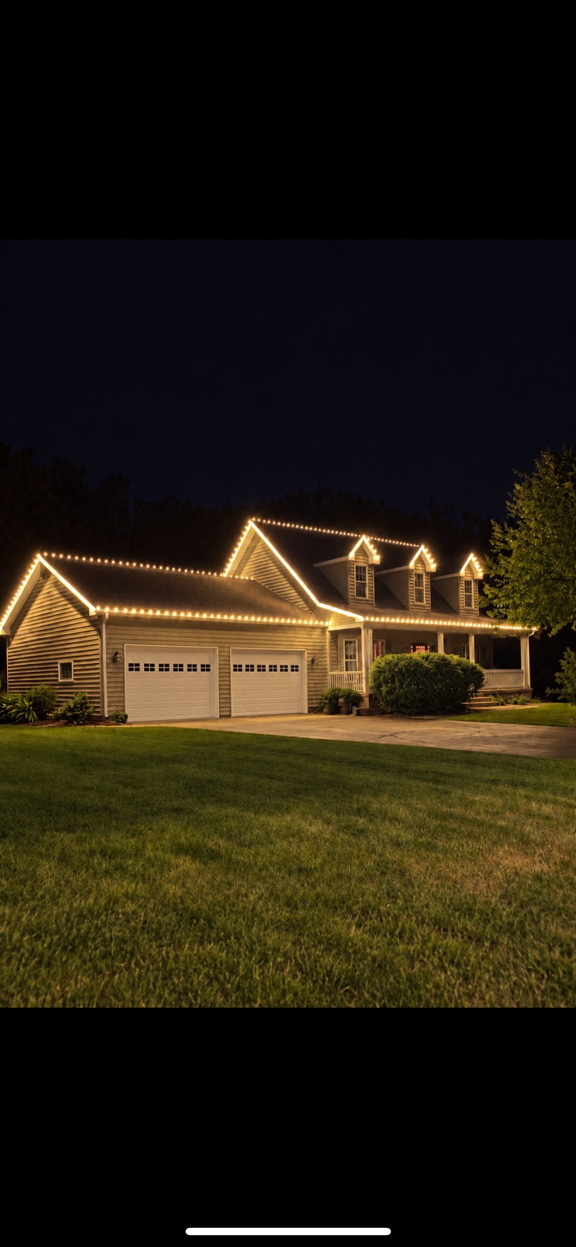 Modern house decorated with white and blue Christmas lights outlining the roofline at night